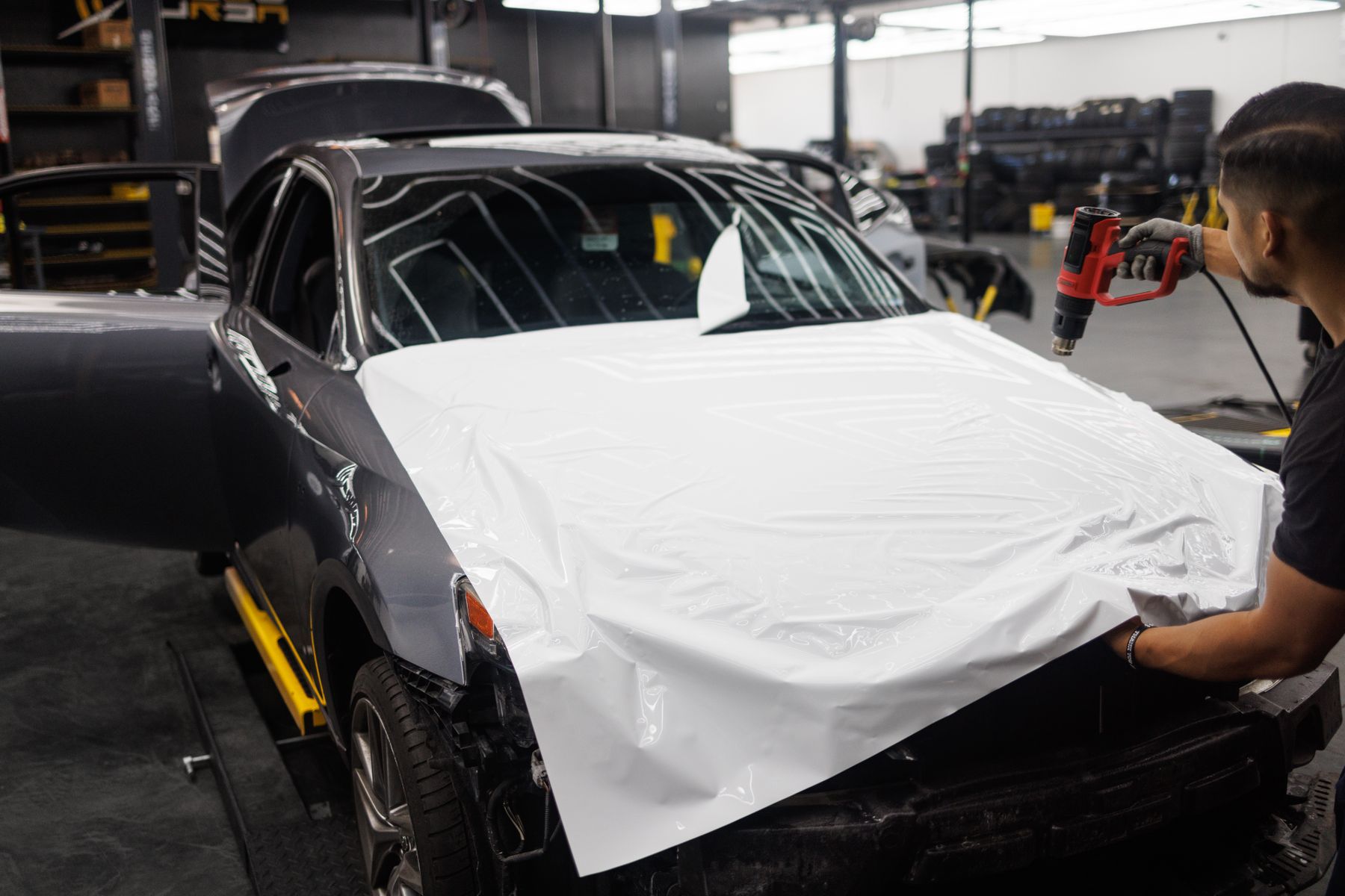 Car being wrapped with white vinyl in a bright automotive workshop